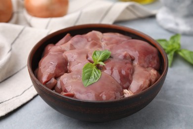 Photo of Bowl with raw chicken liver and basil on light grey table