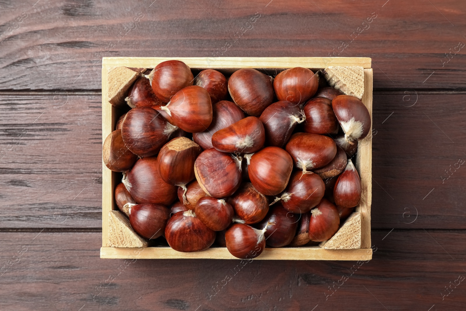 Photo of Fresh sweet edible chestnuts in crate on wooden table, top view