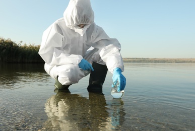 Photo of Scientist in chemical protective suit with florence flask taking sample from river for analysis