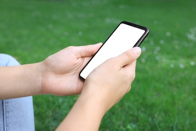 Photo of Woman using smartphone on green grass outdoors, closeup