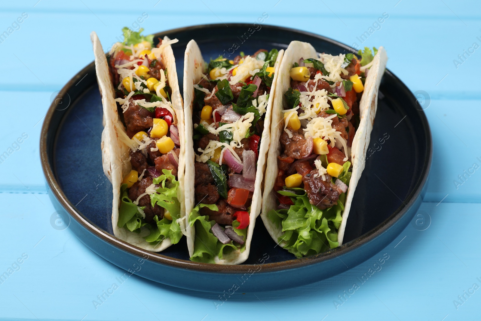 Photo of Delicious tacos with meat and vegetables on light blue table, closeup