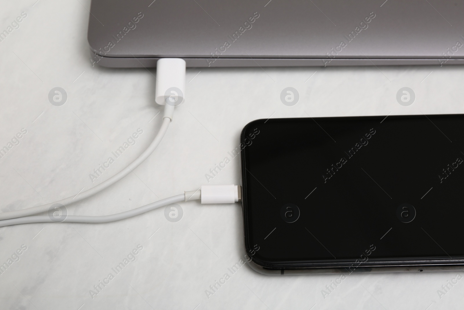 Photo of Smartphone connected with charge cable to laptop on light table, closeup