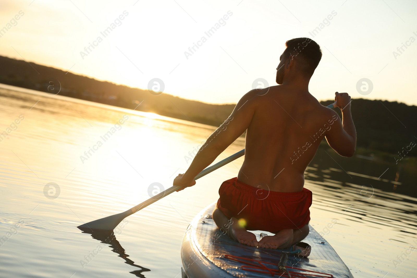 Photo of Man paddle boarding on SUP board in river at sunset, back view