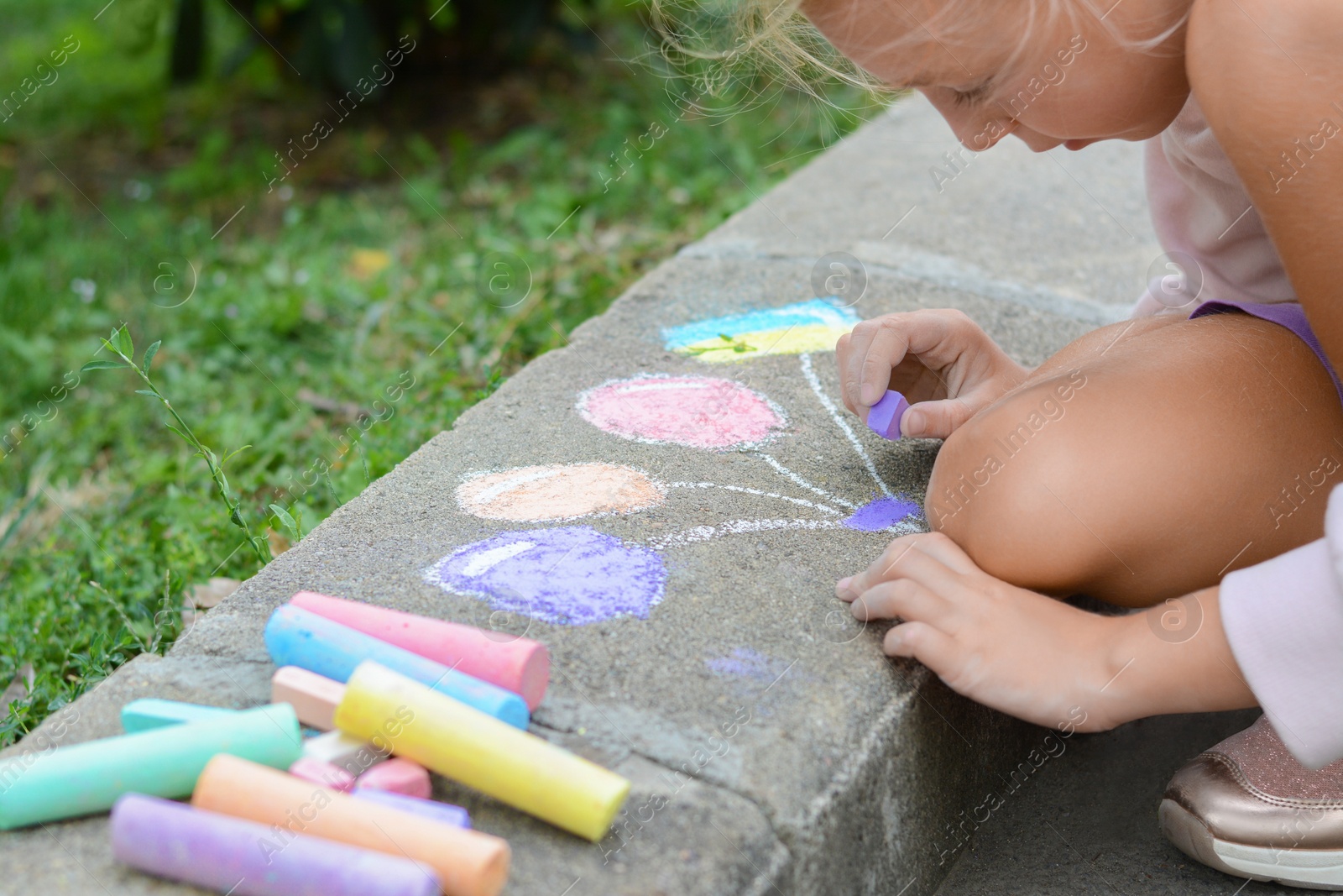 Photo of Little child drawing balloons and ukrainian flag with chalk on curb outdoors, closeup