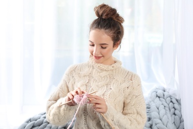Photo of Portrait of beautiful teenage girl in warm cozy sweater knitting at home