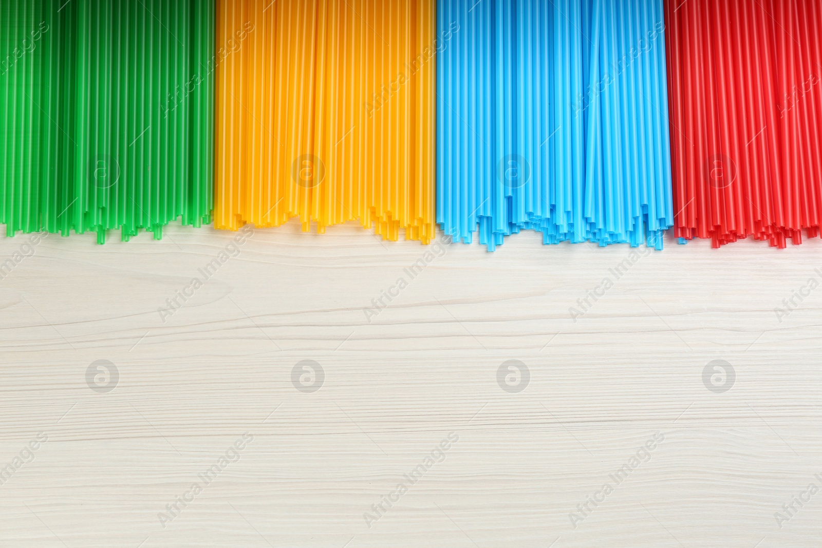 Photo of Colorful plastic drinking straws on white wooden table, flat lay. Space for text