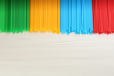 Photo of Colorful plastic drinking straws on white wooden table, flat lay. Space for text