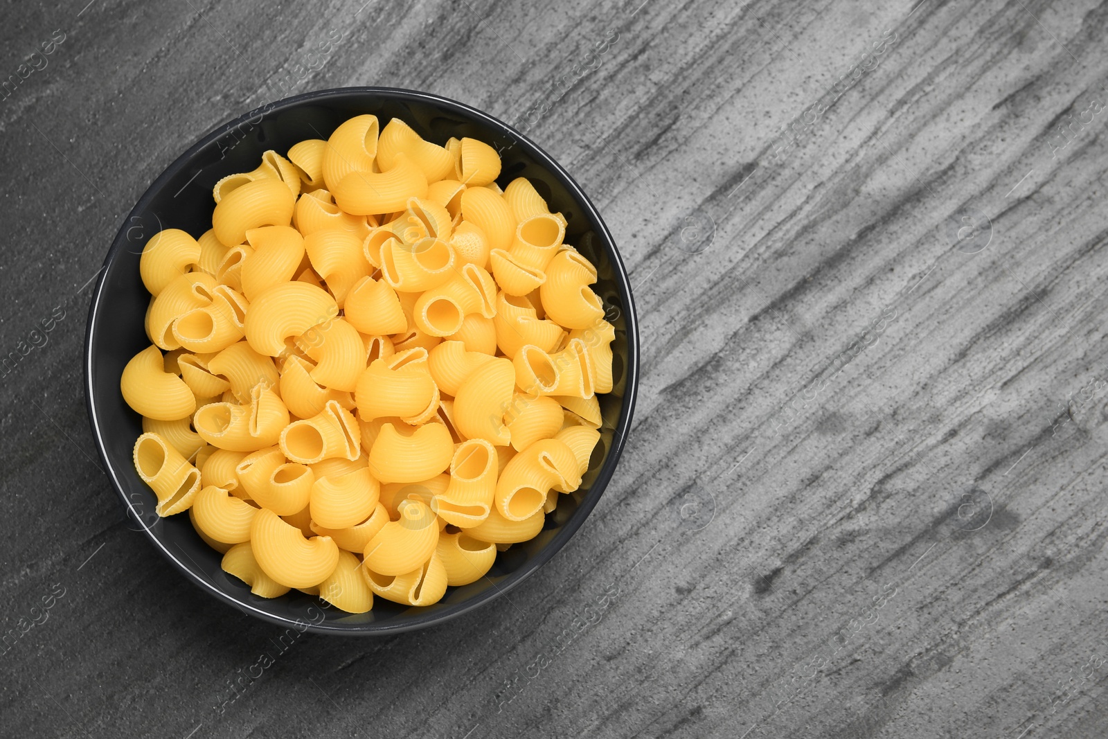 Photo of Raw macaroni pasta in bowl on grey table, top view. Space for text