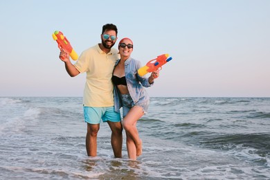 Happy couple with water guns in sea at sunset