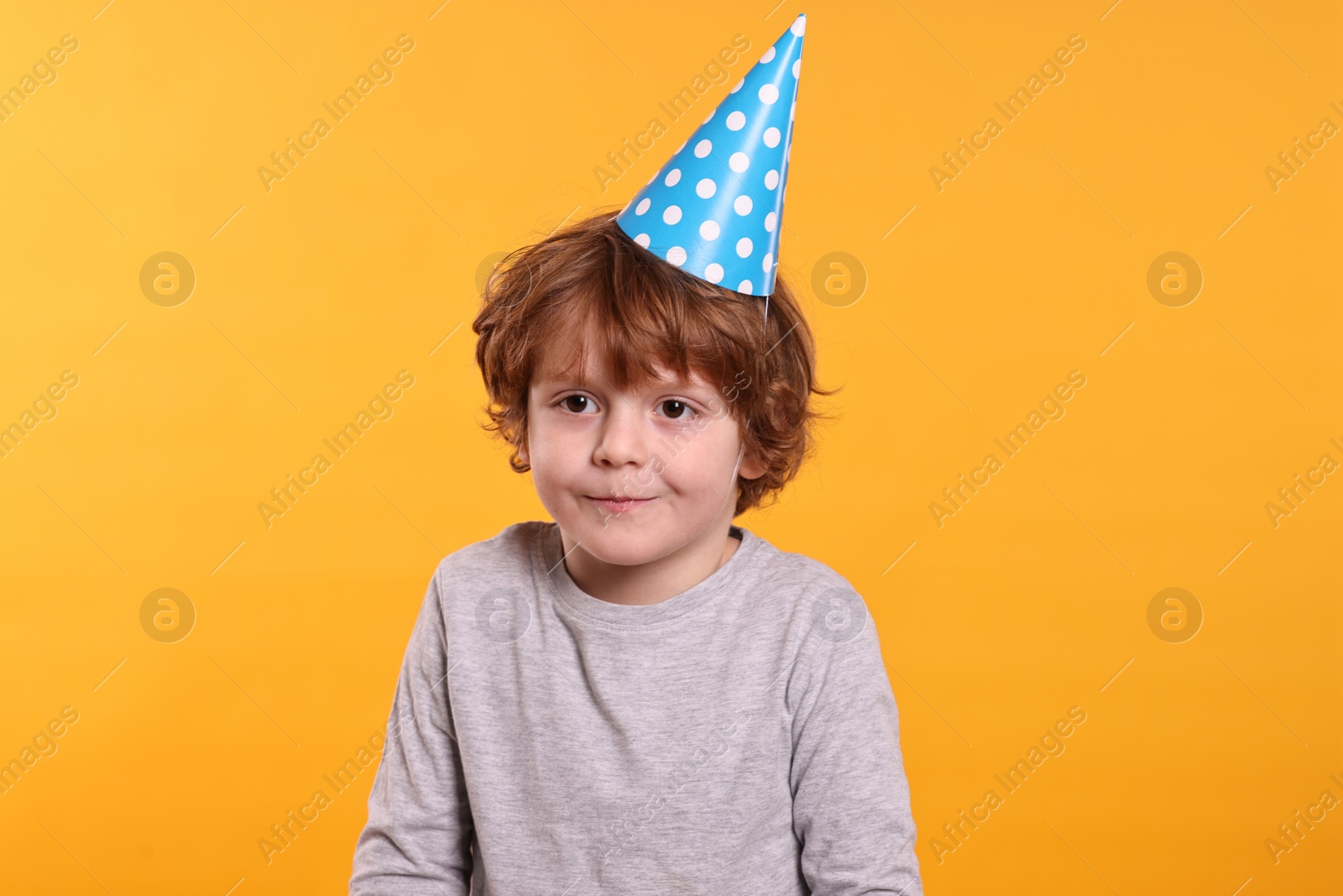 Photo of Birthday celebration. Cute little boy in party hat on orange background