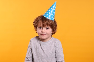 Photo of Birthday celebration. Cute little boy in party hat on orange background