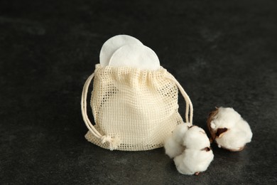 Photo of Cotton pads, bag and flowers on black table, closeup