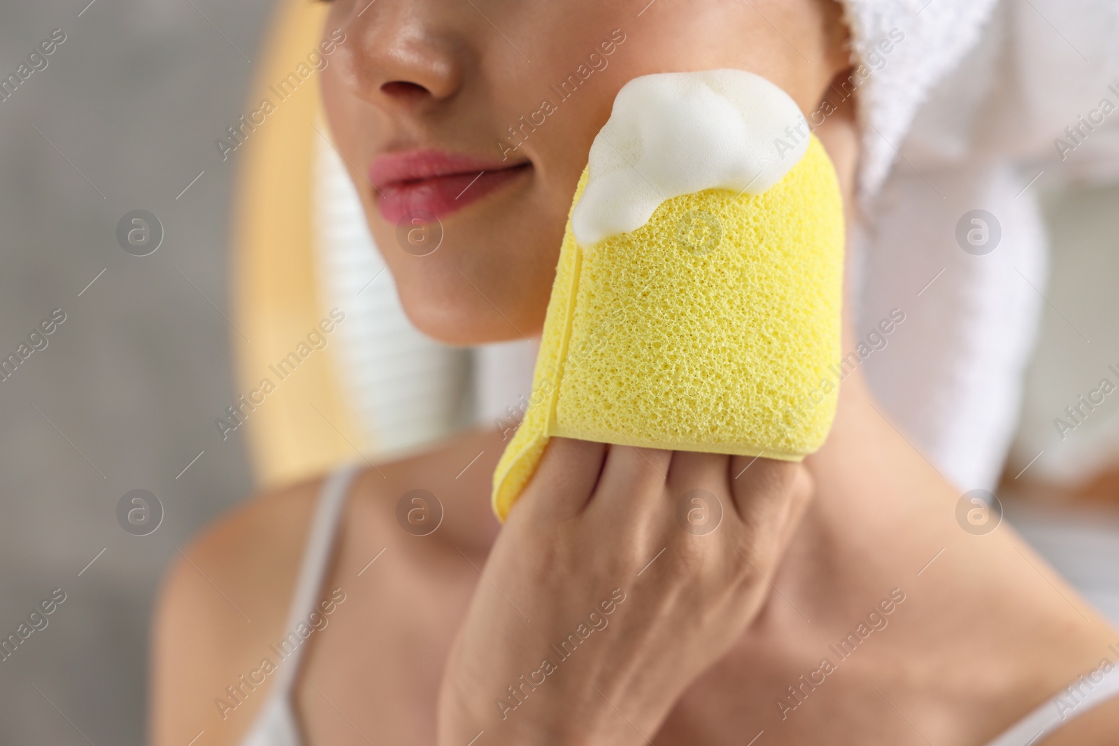 Photo of Young woman washing her face with sponge in bathroom, closeup
