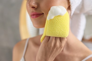 Young woman washing her face with sponge in bathroom, closeup