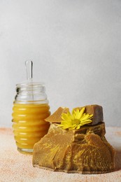 Photo of Natural beeswax blocks, flower and jar of honey on color textured table