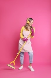 Photo of Beautiful young woman with headphones and mop singing on pink background