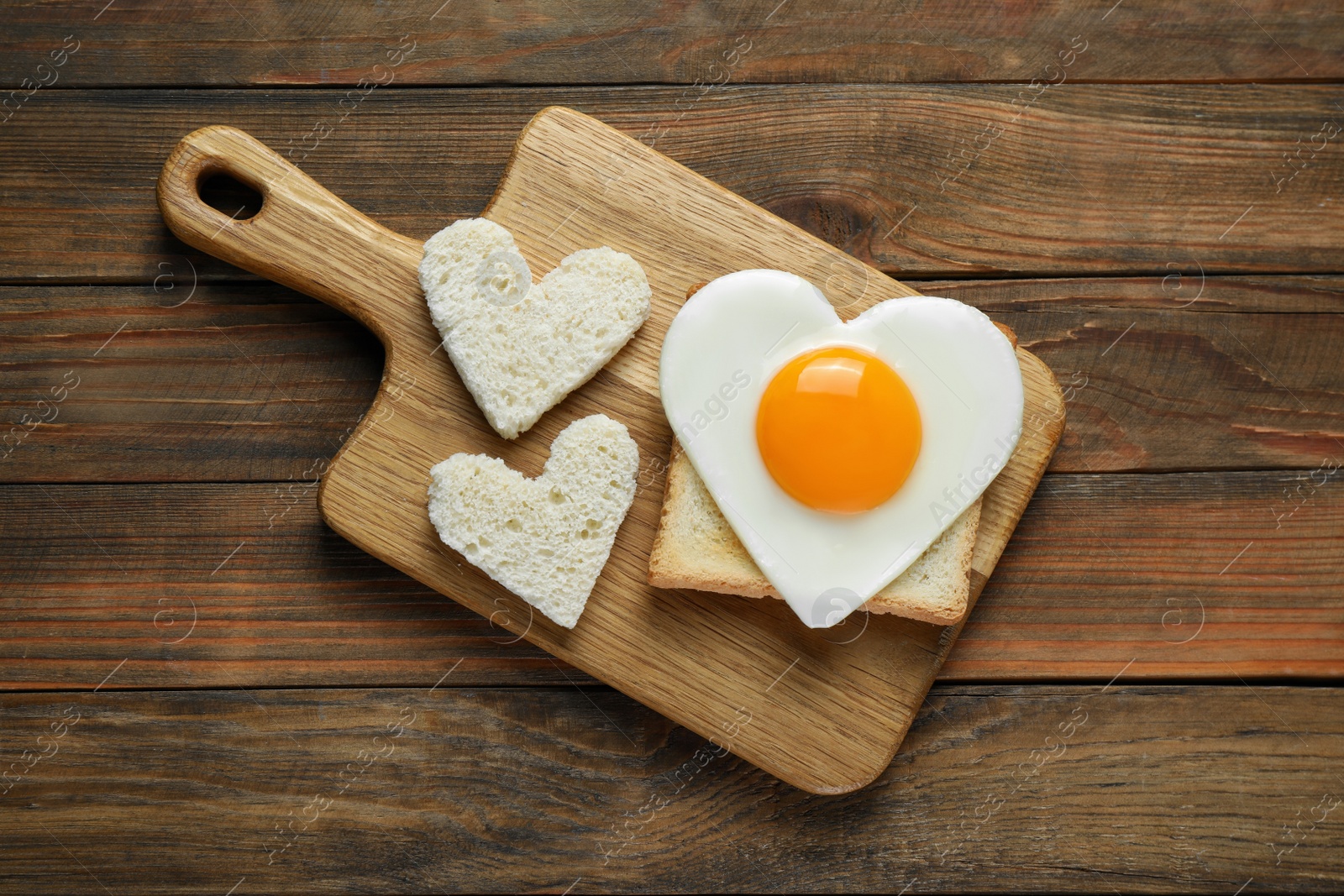 Photo of Heart shaped fried egg with toasts on wooden table, top view