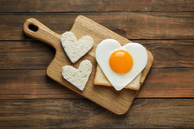 Photo of Heart shaped fried egg with toasts on wooden table, top view