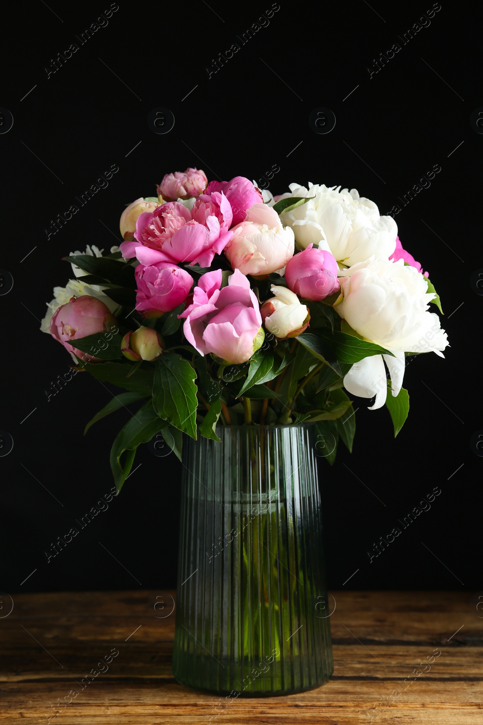 Photo of Bouquet of beautiful peonies in vase on wooden table against black background