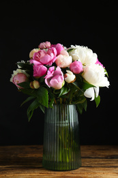 Bouquet of beautiful peonies in vase on wooden table against black background