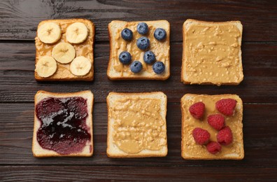 Photo of Delicious toasts with peanut butter, banana, jam and berries on dark wooden table, flat lay