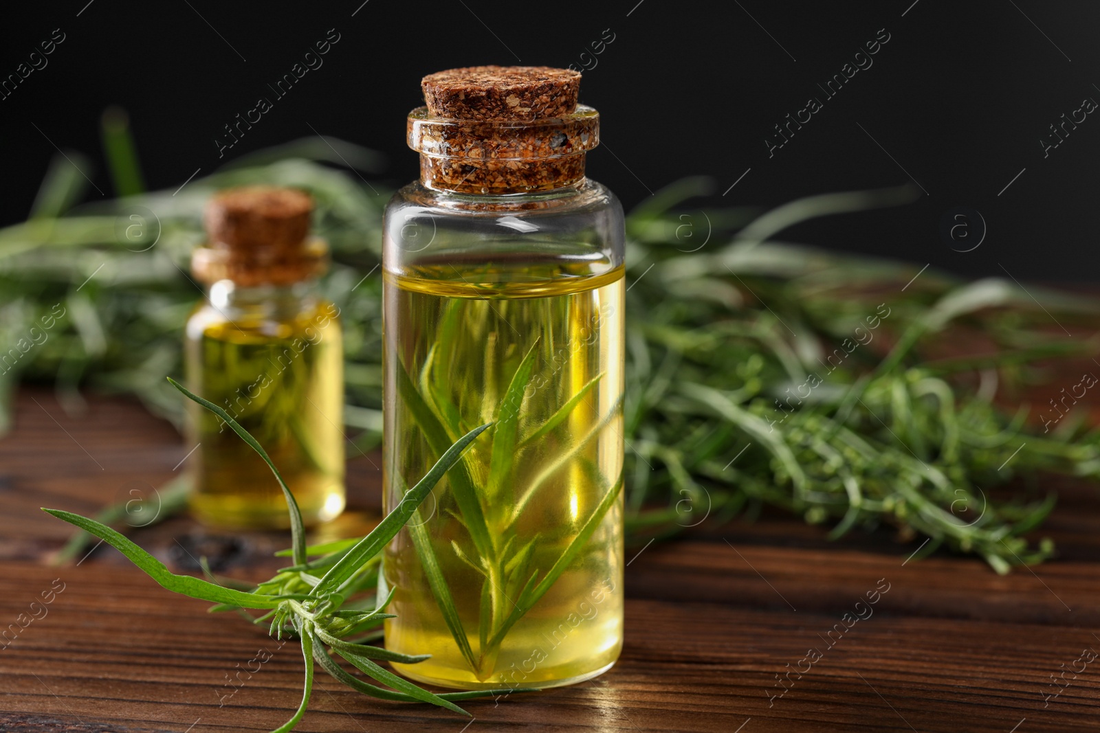 Photo of Bottles of essential oil and fresh tarragon leaves on wooden table, closeup. Space for text