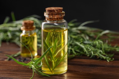 Photo of Bottles of essential oil and fresh tarragon leaves on wooden table, closeup. Space for text