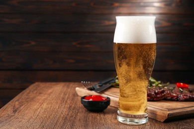 Glass of beer, delicious fried steak and sauce on wooden table. Space for text