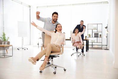 Happy office employees riding chairs at workplace