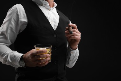 Photo of Man with glass of whiskey smoking cigar against black background, closeup. Space for text