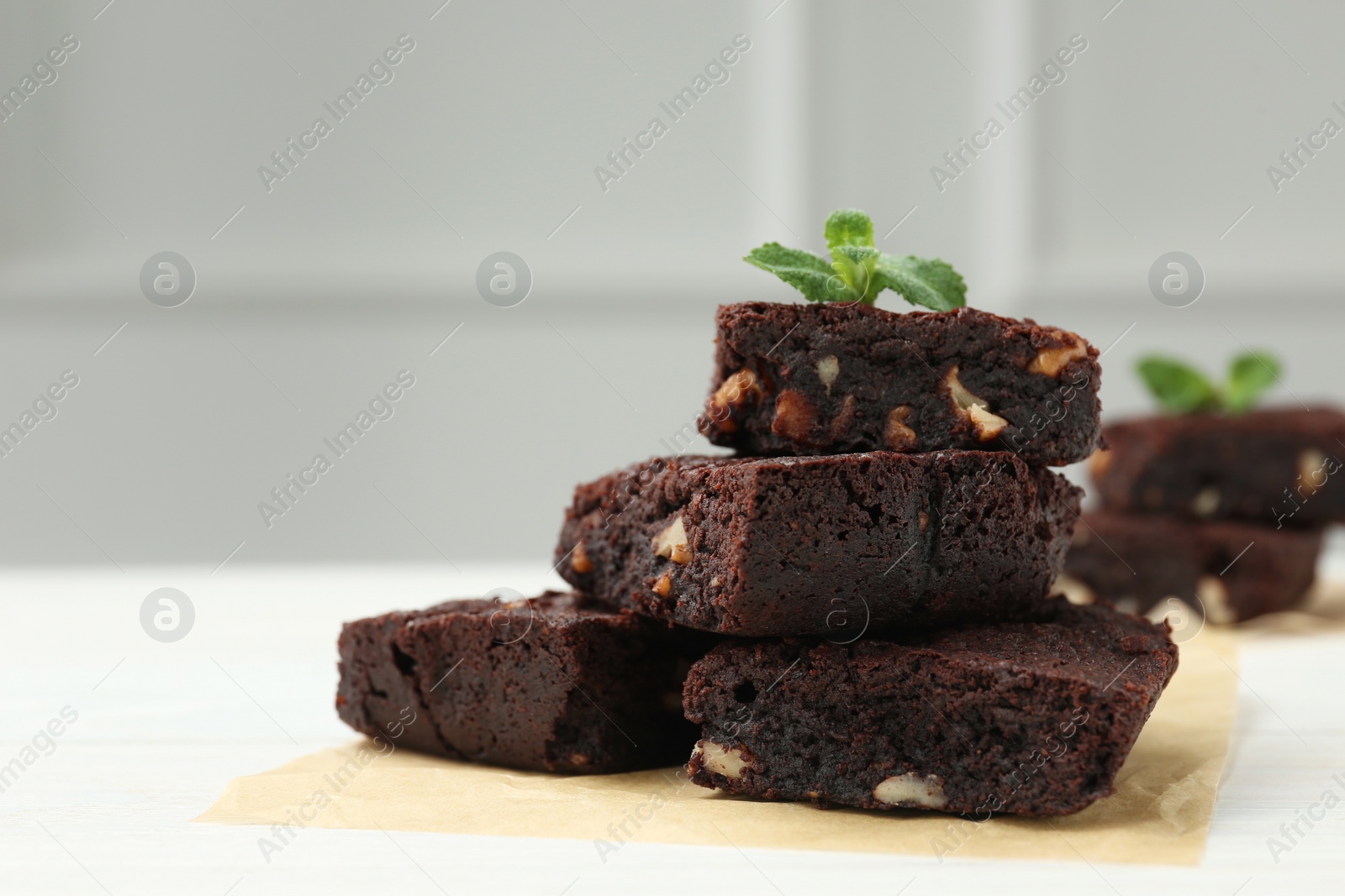 Photo of Delicious chocolate brownies with nuts and fresh mint on white table, space for text