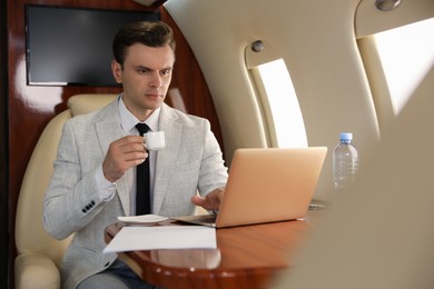 Photo of Businessman with cup of coffee working on laptop at table in airplane during flight