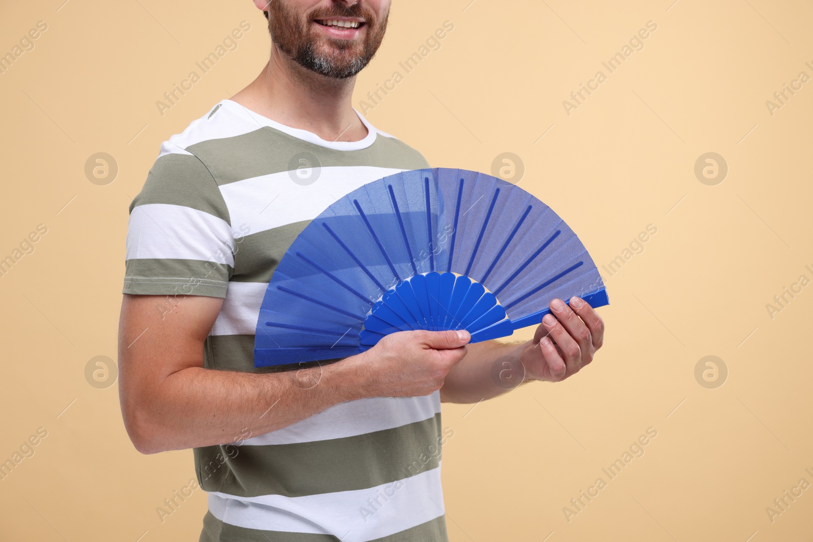 Photo of Man holding hand fan on beige background, closeup