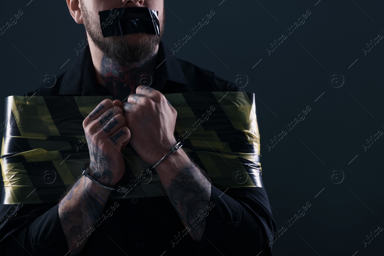 Photo of Taped up and handcuffed man taken as hostage on dark background, closeup. Space for text