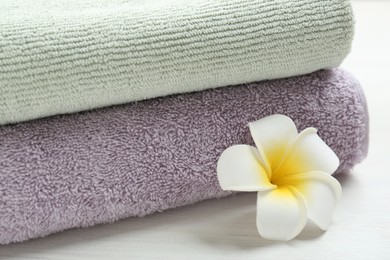 Different folded towels and plumeria flower on white wooden table, closeup