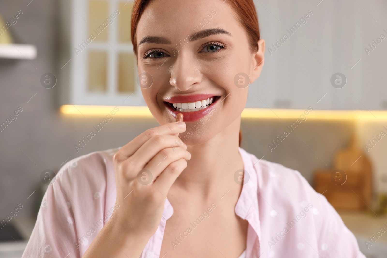 Photo of Beautiful young woman taking vitamin pill at home