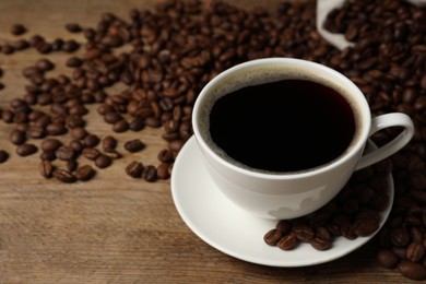 Photo of Cup of aromatic coffee and beans on wooden table, closeup. Space for text