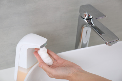 Woman using automatic soap dispenser in bathroom, closeup