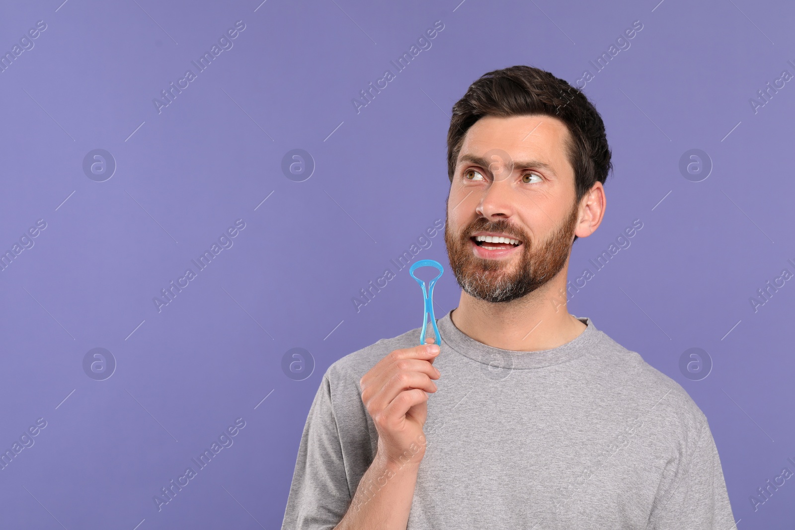 Photo of Happy man with tongue cleaner on violet background, space for text