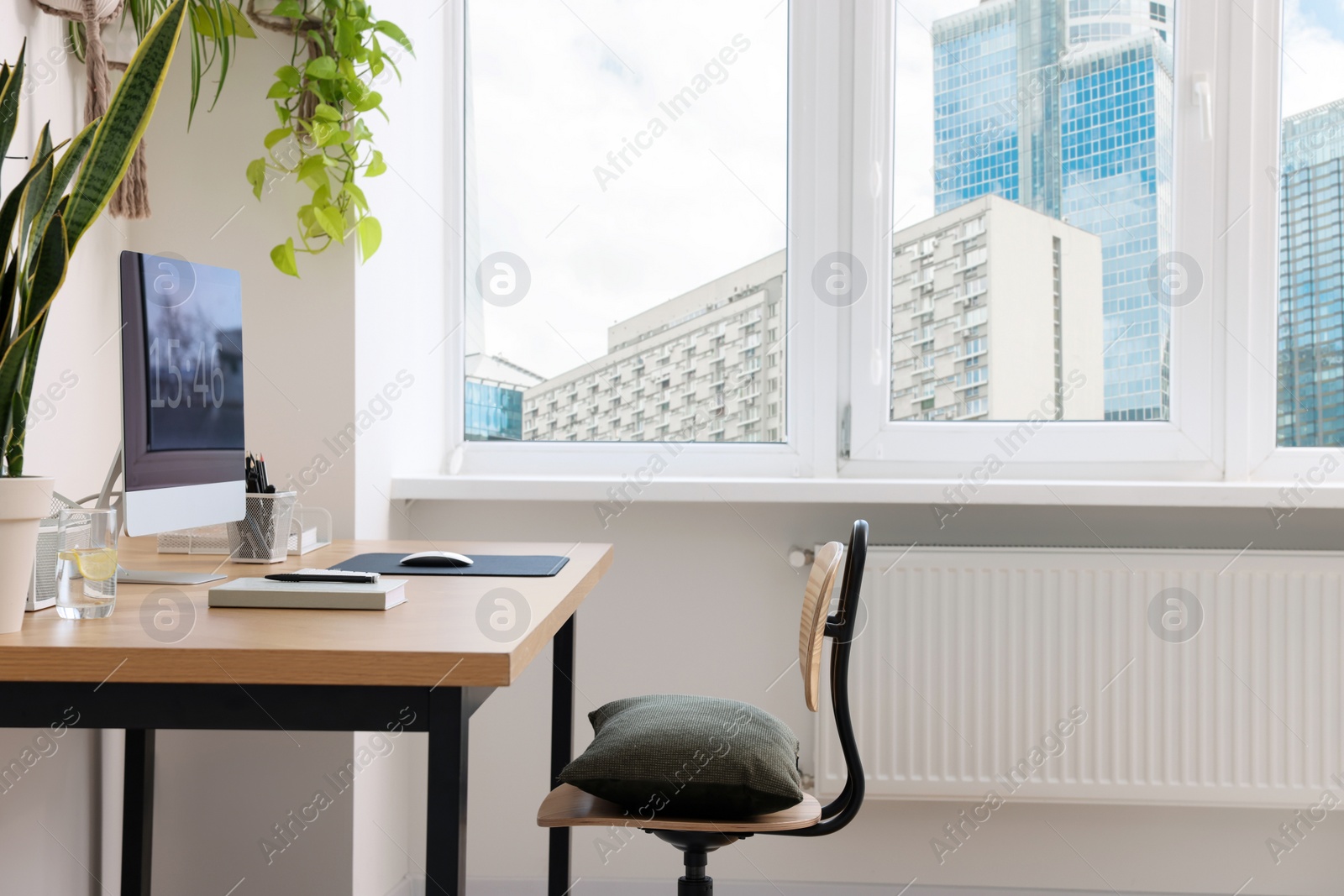 Photo of Cozy workplace with computer, modern furniture and houseplants at home