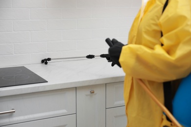 Photo of Pest control worker spraying pesticide on kitchen counter, closeup