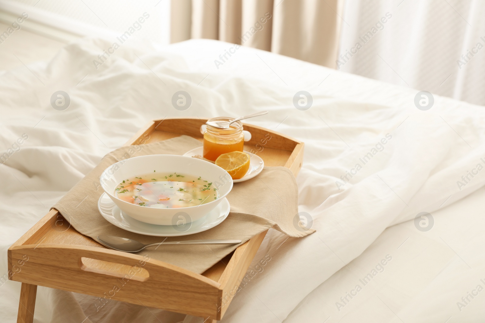 Photo of Tray with bowl of fresh homemade soup to cure flu on bed