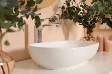 Eucalyptus branches near vessel sink on bathroom vanity. Interior design