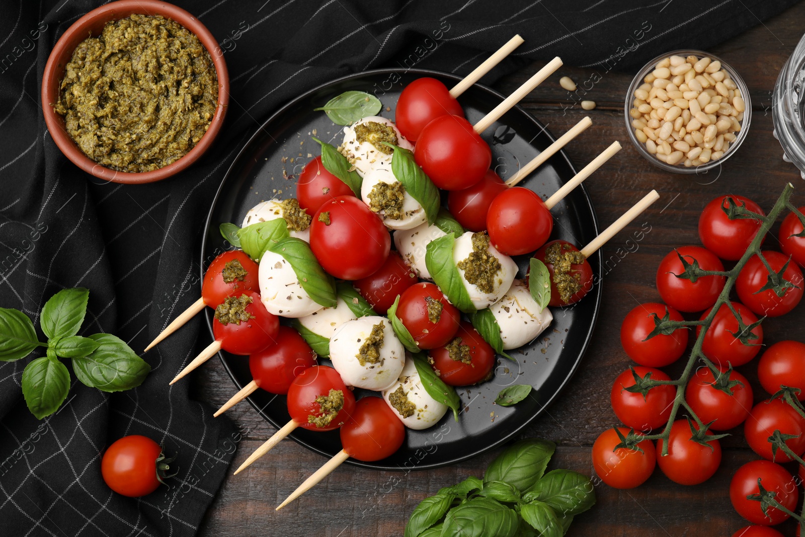 Photo of Caprese skewers with tomatoes, mozzarella balls and basil on wooden table, flat lay