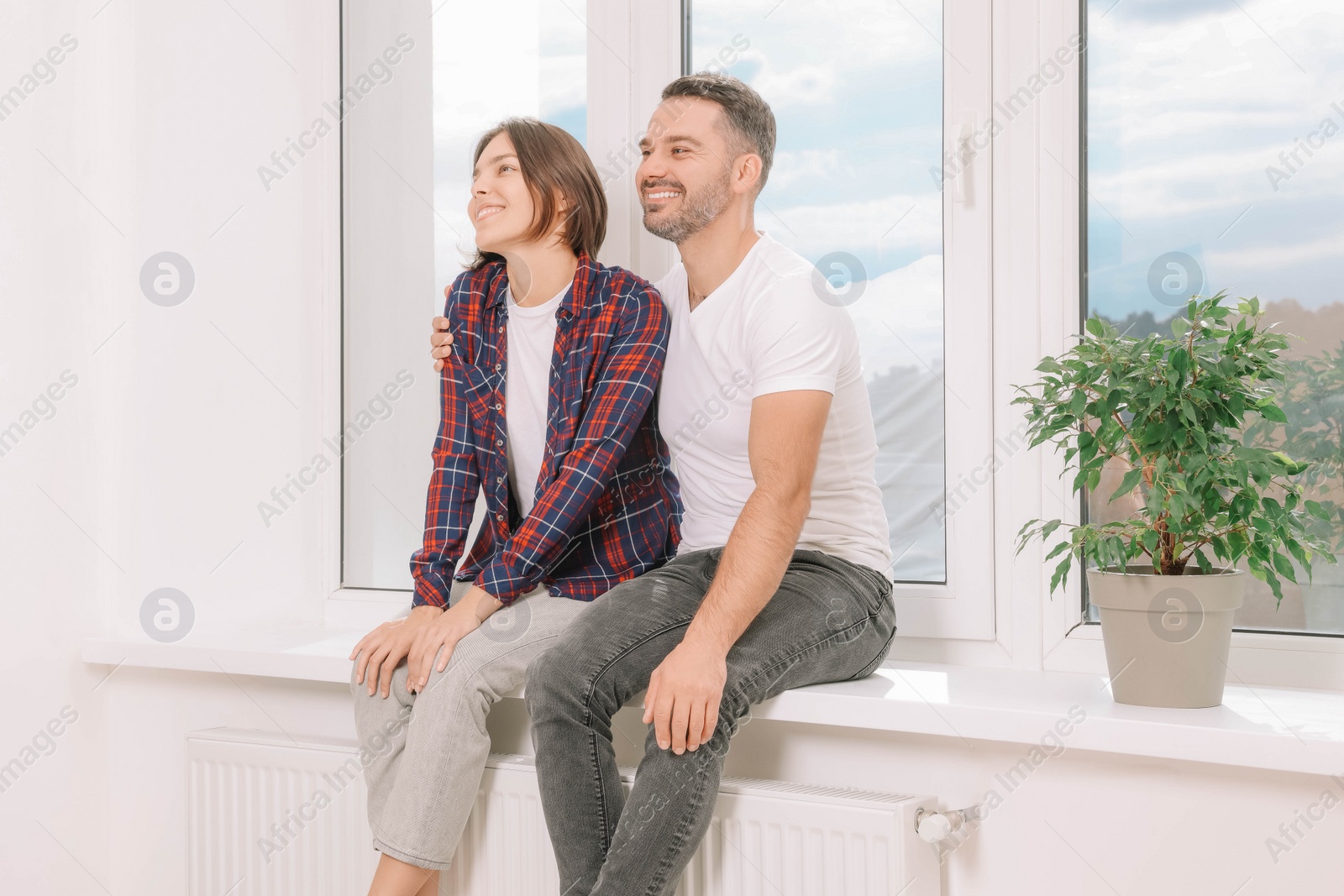 Photo of Happy couple sitting on windowsill in new apartment. Moving day