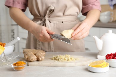 Woman making immunity boosting drink with grated ginger at marble table, closeup