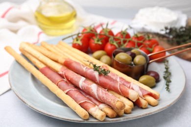 Photo of Delicious grissini sticks with prosciutto and snacks on white table, closeup