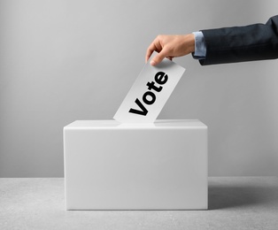 Photo of Man putting his vote into ballot box on table against light background, closeup
