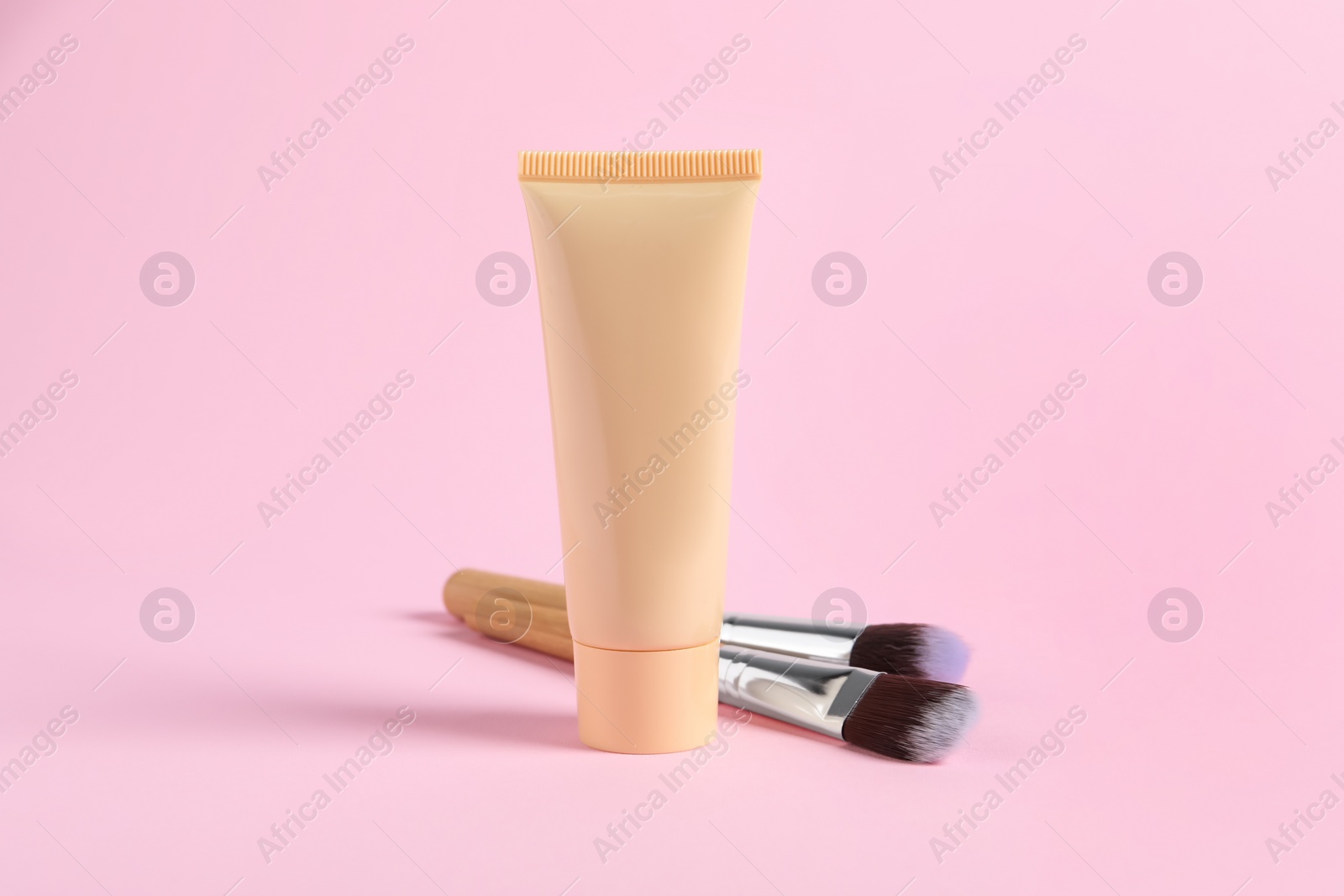 Photo of Tube of skin foundation and brushes on pink background. Makeup product