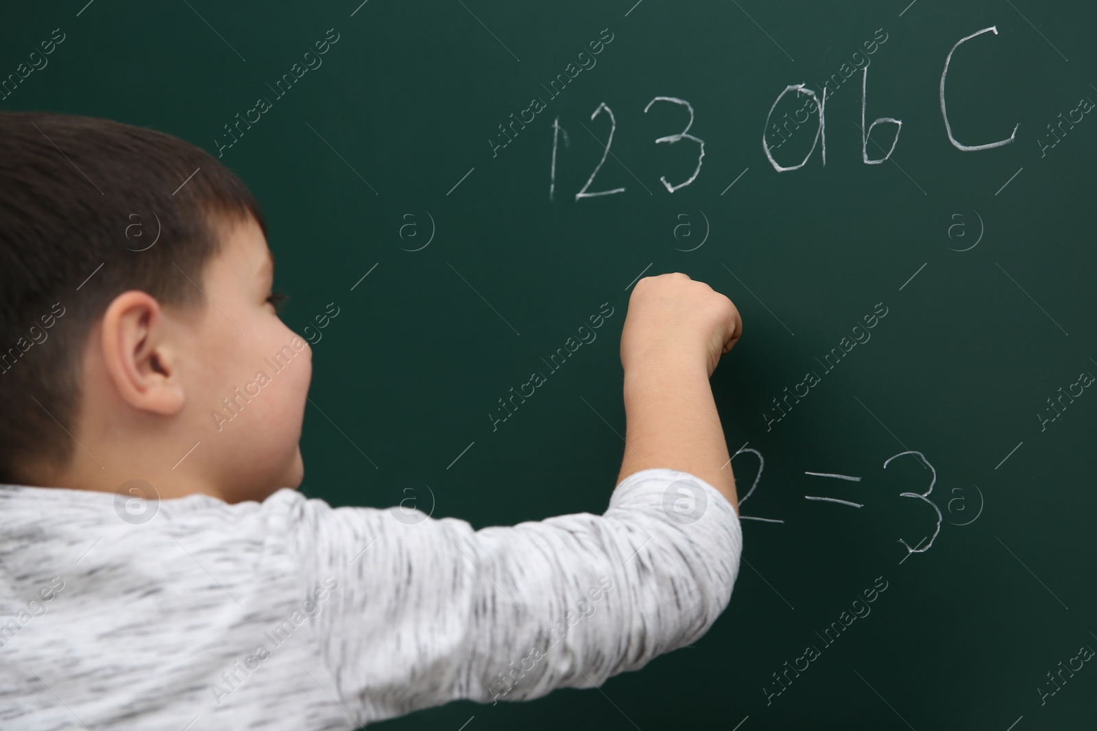 Photo of Little child writing math sum on chalkboard